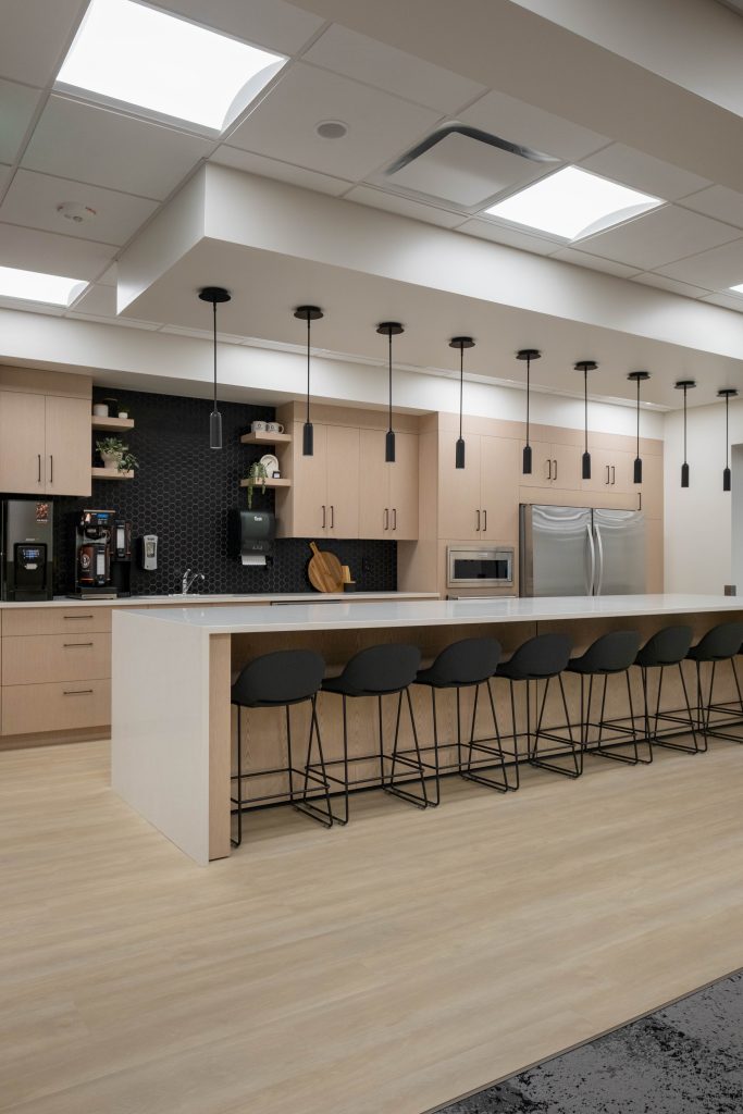 An additional angle from the left of the central island featuring Maple White Quartz with warm blonde cabinetry showcases how bright the space looks. 