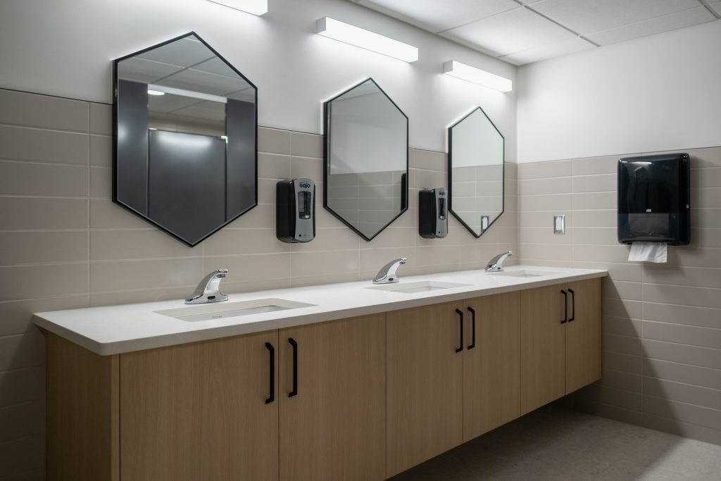 A modern washroom with hexagon-shaped geometric mirrors features a counter with Maple White Quartz provided by CNG Stone paired with light wood cabinets.  